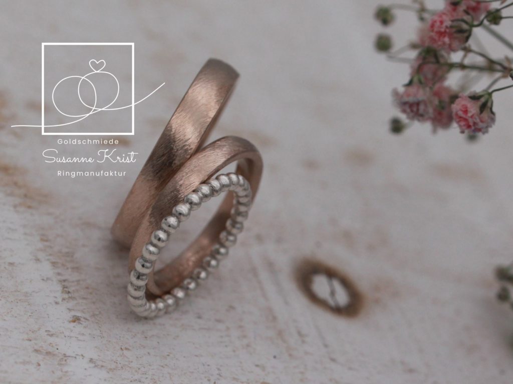 Auch sehr kombinationsfreudig: Schlichte Trauringe aus Haselnussgold mit weißem Kugeldring dazu.
